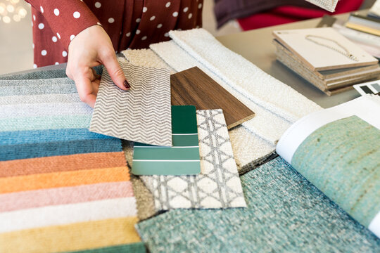 Close up of Interior designer choosing materials for home renovation. Woman matching samples the color of the walls to the parquet board, fabrics swatches. House decoration renovation