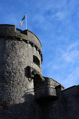 Irish flag atop old castle tower shining in the sun with blue copy space background + clouds. Irish...