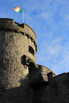 old castle tower with Irish flag atop it shining in the sun with blue copy space background. Irish medieval castle travel shot, background, wallpaper or screensaver with text space -King John's Castle