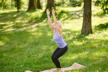 Middle aged woman doing yoga outdoor barefoot in park in Revolved Chair Pose.Parshva (Side). The concept of stretching, pilates, yoga, healthy lifestyle.Yoga practice in nature.