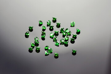 Lot of small calibrated round faceted deep grass green color tsavorite garnet gemstone settings. Dark gradient reflective background. High contrast. Poor quality faceting. Mass market goods.