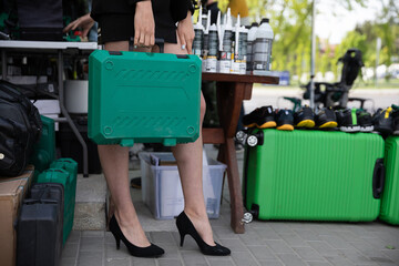 A girl on stilettos holds a plastic green tool case.