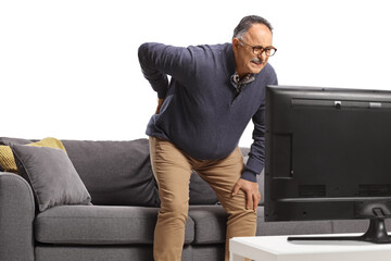 Mature man with back pain getting up from a sofa in front of tv