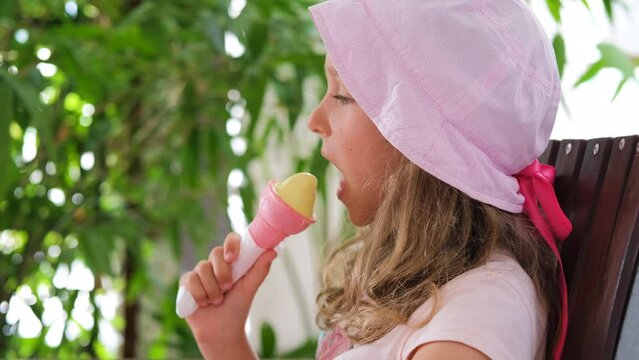 Happy little girl eating ice cream in pink crispy cone in summer day, slow motion
