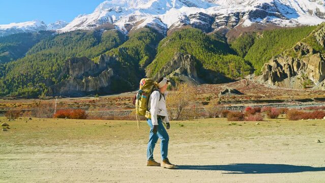 Full body side view of adult trekker walking on trail with snow capped Annapurna mountain range in the distance, Nepal