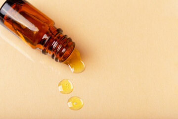 Yellow liquid spilled from an amber cosmetic bottle. Essence, oil, serum, emulsion. Natural organic cosmetics. Beige background with copy space. Selective focus