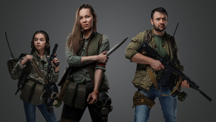 Studio shot of female killer with man and young girl in setting of post apocalypse.