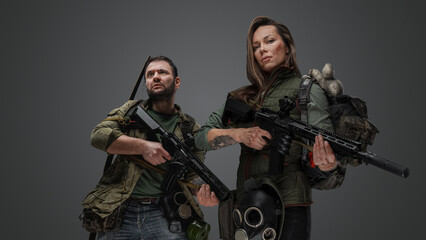 Studio shot of post apocalyptic couple survivors with guns against gray background.
