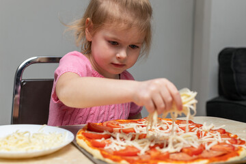 Small child cooking at home sitting at the table. Little girl making pizza in the kitchen.