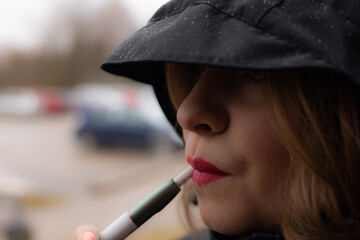 A woman with red lips is smoking an electronic cigarette. Beautiful young woman under the hood. Young girl with beautiful red lips