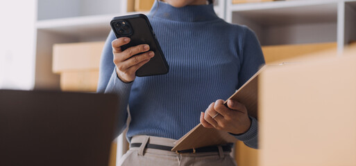 Startup SME small business entrepreneur of freelance Asian woman wearing apron using laptop and box to receive and review orders online to prepare to pack sell to customers, online sme business ideas.