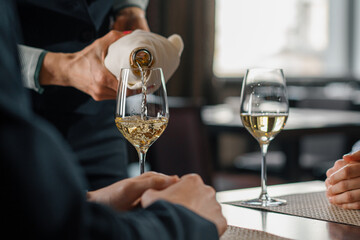 A date in a hotel restaurant a man and a woman drink white wine in glasses the waiter pours wine from a bottle