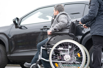 Fototapeta na wymiar A woman helps aphysical disabled person to get into the car