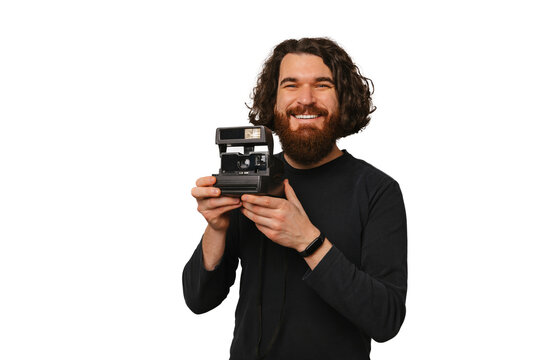 Smiling bearded man is holding a vintage instant camera near his face.