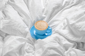 Blue cup and saucer with cappuccino on a white bed