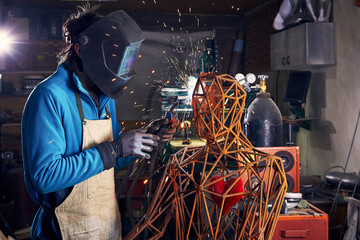 Sculptor is using arc welding to assembly metal sculpture in protective mask