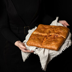 Homemade square cake with cuts on towel in hands of woman. Fresh baked goods with filling. Puff pastry. Crunchy crust. Black background. Side view. Copy space.