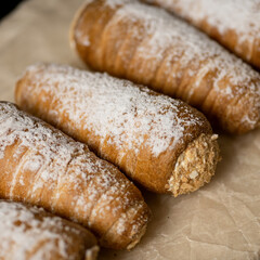 Tubes with cream on parchment for baking sprinkled with powdered sugar. Dessert made from puff pastry with custard protein or butter cream. Sweet homemade cake for tea. Close-up. Soft focus. 