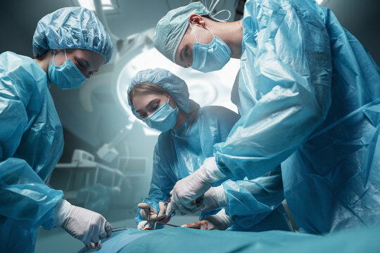 Shot of three surgeons dressed in robes and masks with patient in operating room.