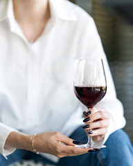 Woman with glass of red wine in her hands. Wine tasting. Rest, relaxation. Blurred figure of woman in white shirt in background. Front view. Soft focus. 