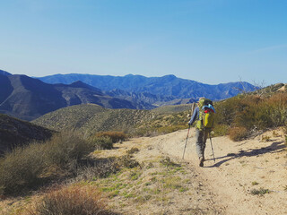 Male backpacker hiking through the California desert with mountains and desert plants