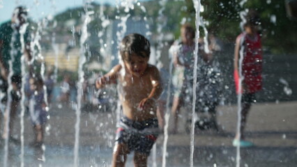One happy small boy running toward water jets at outdoor park during summer vacations