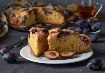 Homemade open pie with plums and cup of tea on dark gray background