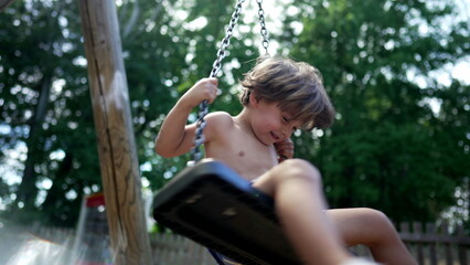 One small boy having fun at playground swing outdoors during summer day shirtless kid. Child spinning outside having fun