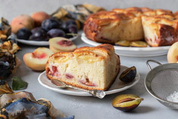 Homemade pie with plums and peaches, sprinkled with powdered sugar on gray background