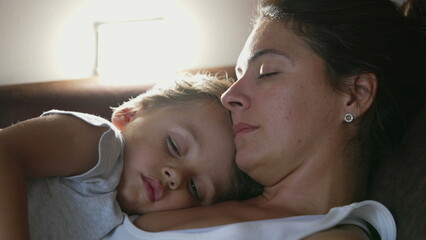 Obraz na płótnie Canvas Mother and child napping together lying on couch. Candid authentic parent asleep with son