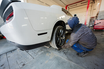 Mechanic in service repair station working with muscle car.  Man worker jacks up the car to diagnose the chassis.