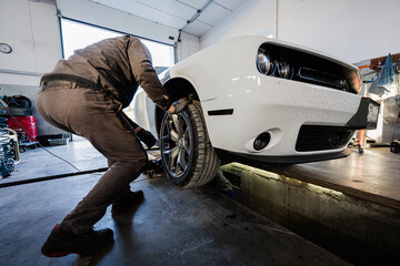 Mechanic in service repair station working with muscle car.  Inspects the running part of the wheel.