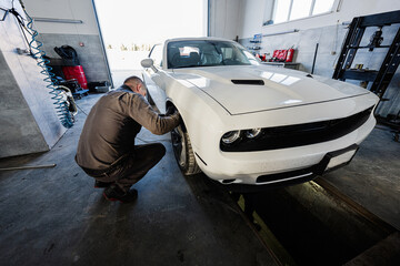 Mechanic in service repair station working with muscle car.  Man worker diagnose the chassis.