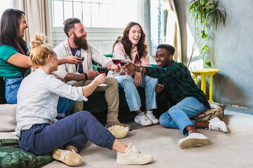 Multiethnic group of happy friends toasting for home aperitif with red wine on sofa