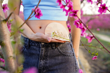 unrecognizable woman in spring with ostomy bag and pink flowers. colon cancer day