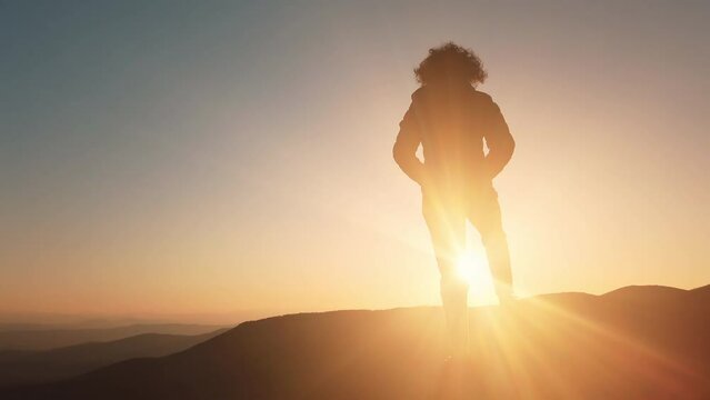 A young woman hiker in a jacket standing on peak in the mountains enjoying sunset, amazing view of clouds iover valey