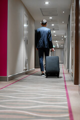 A man with a suitcase walks down the hotel corridor a back view of a businessman on a trip