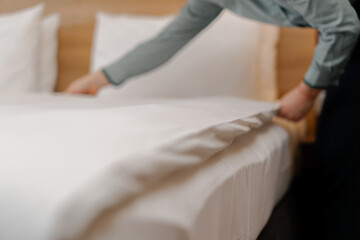 A housekeeper in a uniform makes a bed preparing a luxury hotel room for guests cleaning and travel concept