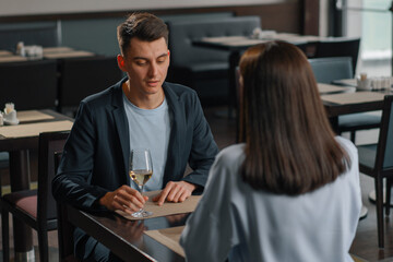 A date in a hotel restaurant, a man and a woman drink white wine in glasses the face of a serious man