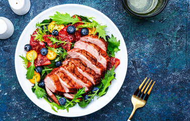 Duck salad with grilled breast with red orange, kumquat, blueberry and chard, frisse, mizuna and arugula leaves on blue table background, top view