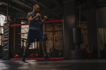 Fototapeta na wymiar A boxer in the gym who fights with the shadow practices punches