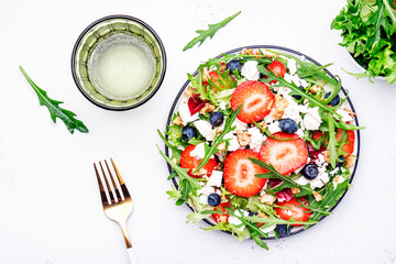 Strawberry and herbs healthy salad with arugula, blueberries, soft white feta cheese and walnuts, white kitchen table, place for text. Fresh useful dish for healthy eating