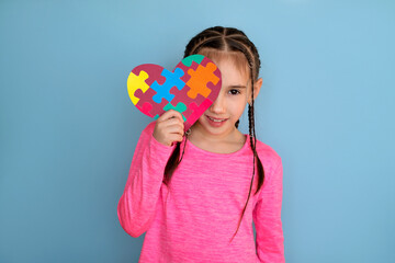 A beautiful stylish girl gently holds a heart-shaped card with puzzles, covering part of her face. The unity of humanity in relation to special people, unlike others