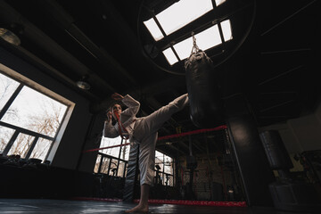 Obraz na płótnie Canvas A girl in a kimono exercises with a punching bag in the gym while learning karate martial arts