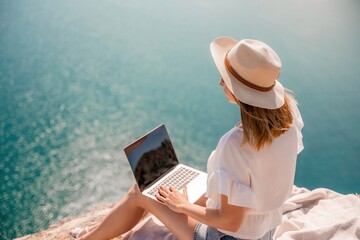 Freelance women sea working on the computer. Good looking middle aged woman typing on a laptop keyboard outdoors with a beautiful sea view. The concept of remote work.