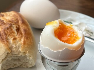Simple rustic breakfast - soft semi cooked egg with plain pastry bun on simple white plate. Cheap, easy and healthy breakfast.