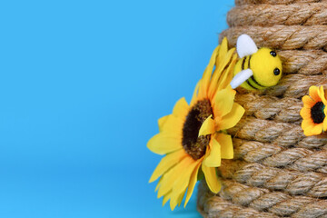 Cute felt bee on rope beehive decoration in front of blue background with copy space