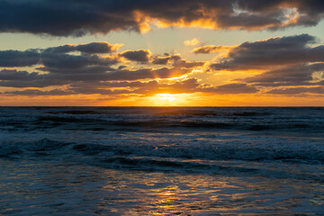Evening landscape of sea water waves crushing on sandy beach at sunset