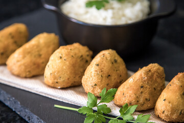 Bolinhos de bacalhau, very famous in Portuguese gastronomy. Fried dumpling, cod dumpling, fish, salted cod fritters, bacalao bunuelos. Codfish cake served with white rice on a dark background.