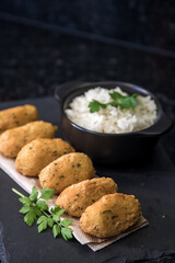 Bolinhos de bacalhau, very famous in Portuguese gastronomy. Fried dumpling, cod dumpling, fish, salted cod fritters, bacalao bunuelos. Codfish cake served with white rice on a dark background.